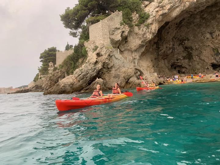 Teens sea kayaking beneath the rocky coast near Dubrovnik