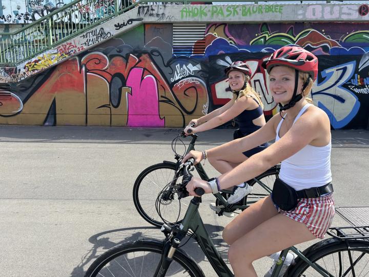 Two girls on a bike tour past a graffiti wall in Vienna