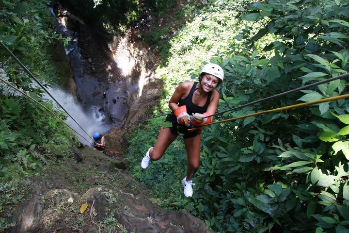 A girl abseiling down a rock face beside a waterfall