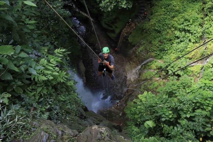 A teen abseiling into a jungle canyon beside a waterfall