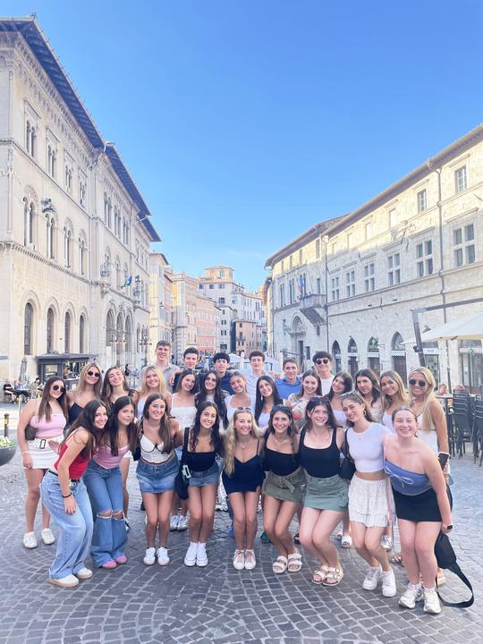 A big group of teens posing on a street lined with old buildings in a European city