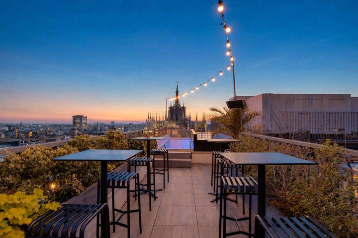 Rooftop bar of a hotel in Milan at sunset, with the cathedral spires in the distance
