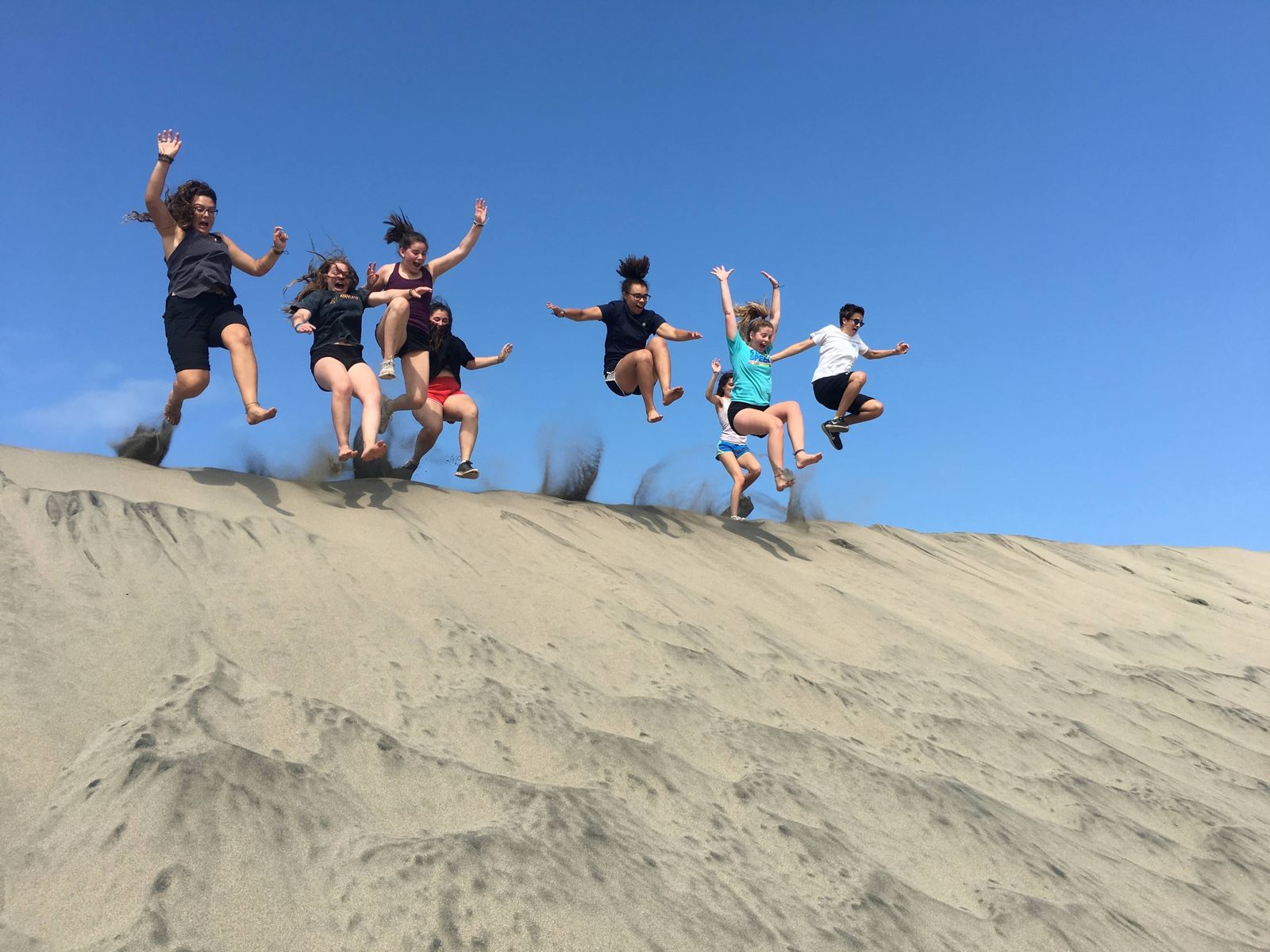 Teens jumping off the top of a sand dune