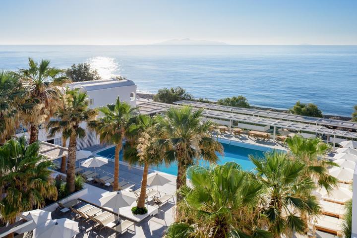 Hotel pool among palm trees on Santorini, looking out to sea
