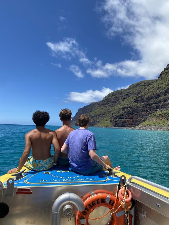 Teens on a boat beneath green sea cliffs
