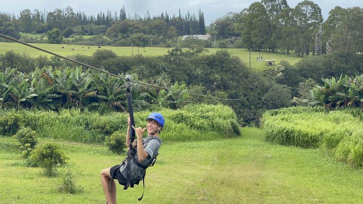 A teen on a zipline over green fields on the Big Island