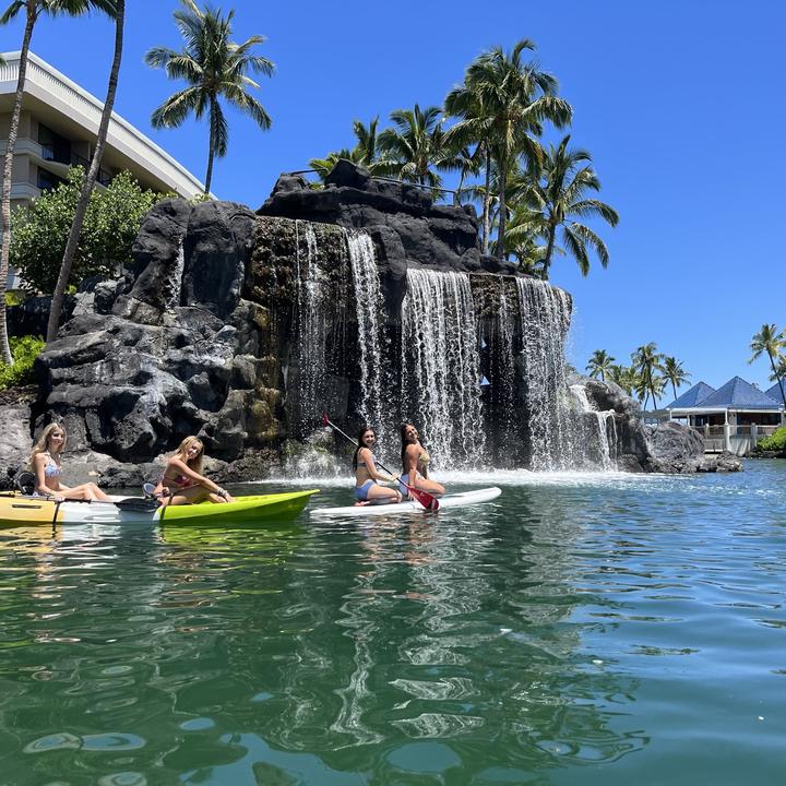 Teens paddling in a resort lagoon with a waterfall