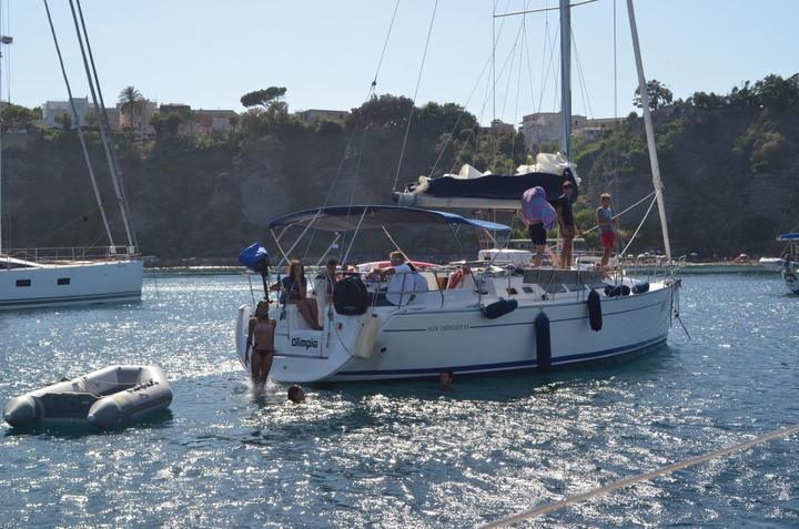 A yacht at anchor in a bay, with the dinghy alongside