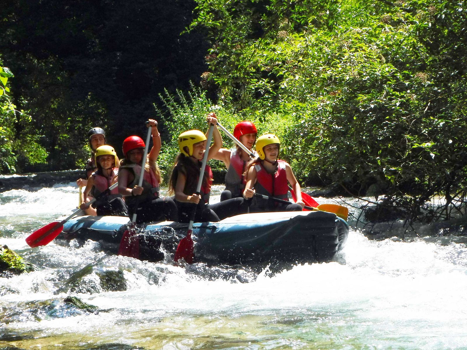 Teens in helmets paddling a raft through white water
