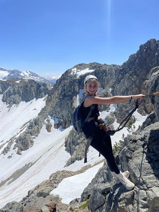 A teen on a via ferrata above snowy peaks