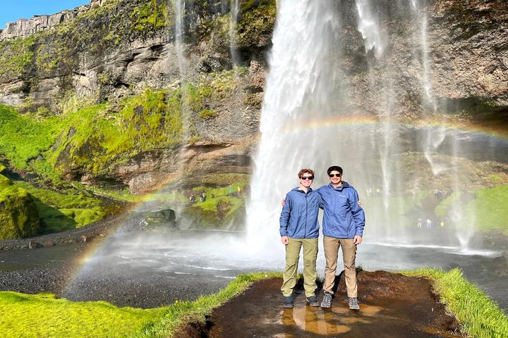 Two teens beneath a waterfall with a rainbow in Iceland