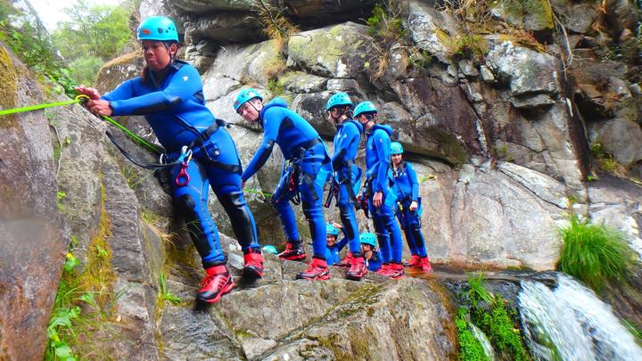 A group canyoning down a waterfall in wetsuits and helmets