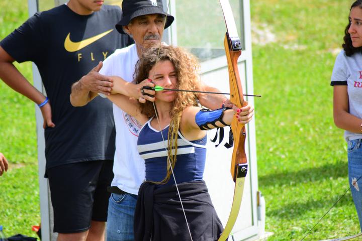 Coach helping a camper draw a bow at archery