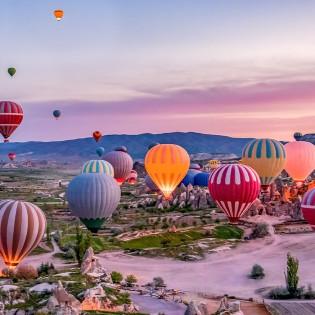 Cappadocia's valleys at sunrise, with hot-air balloons in the sky