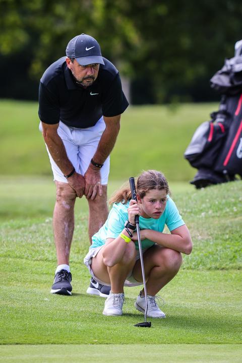 A coach and a young golfer reading a putt together