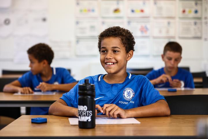 A smiling young camper in Chelsea kit during a classroom session
