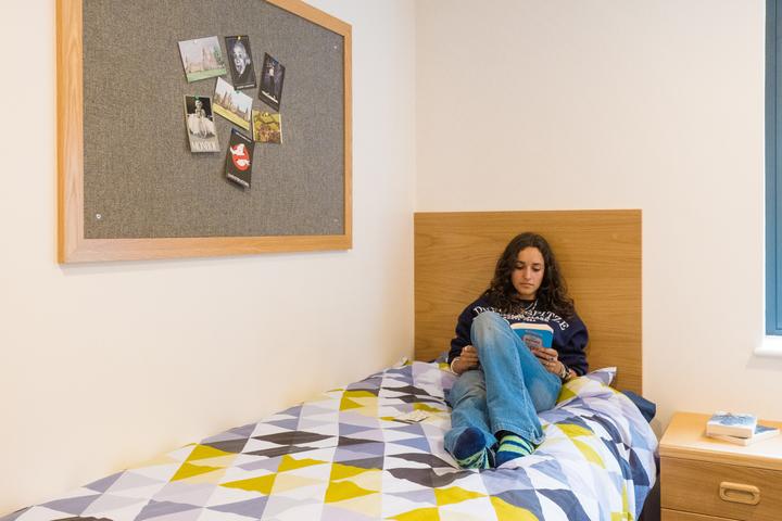A camper reading on her bed in a single boarding-house bedroom
