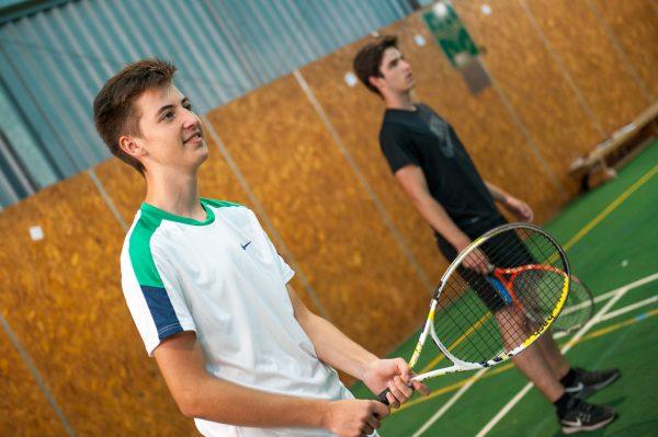 Two teenage boys with tennis rackets, smiling on an indoor court