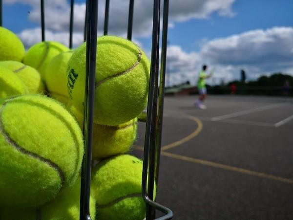A basket of tennis balls beside the court, a player in the background