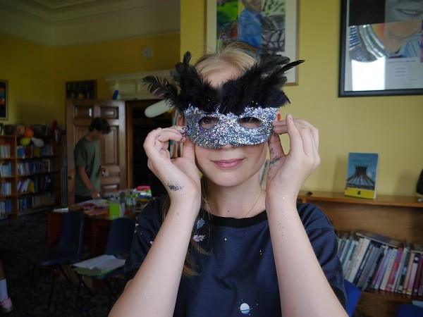 A student trying on the feathered mask she made