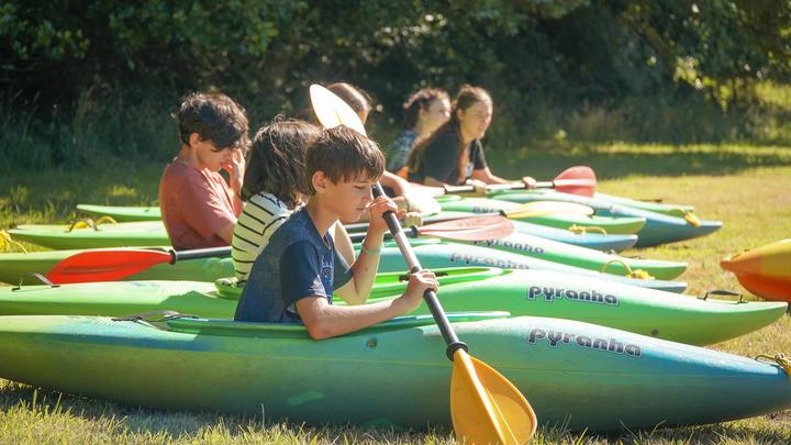 Campers in kayaks on the grass learning to paddle