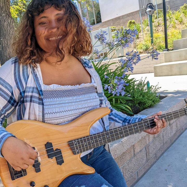 Camper playing bass guitar outdoors on campus