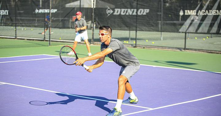 An adult player stretching for a low volley on a hard court