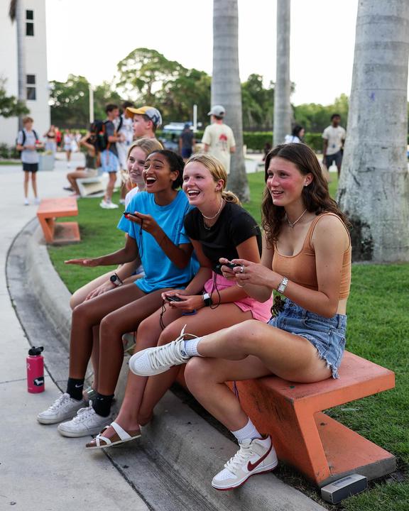 Four girls laughing together on a bench on campus