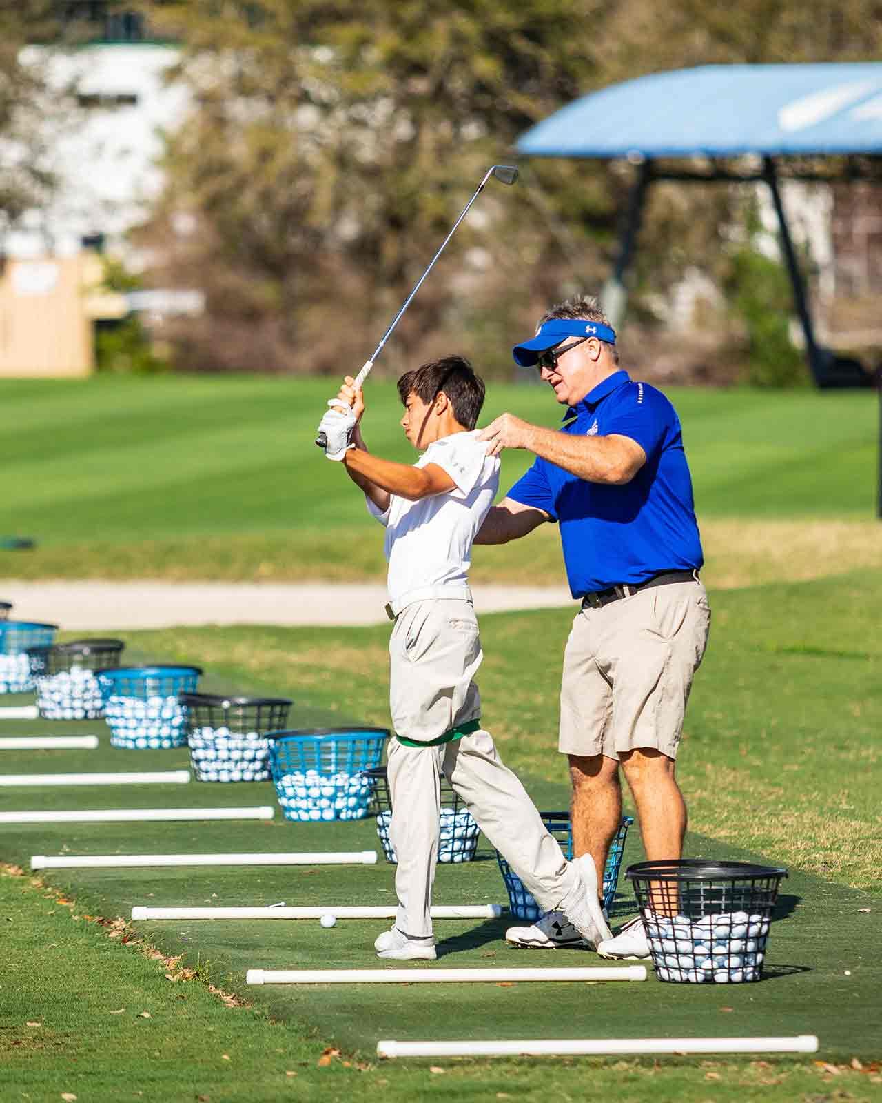A coach helping a boy with his swing on the driving range