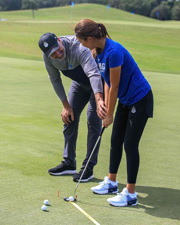 A coach checking a girl's alignment on the putting green