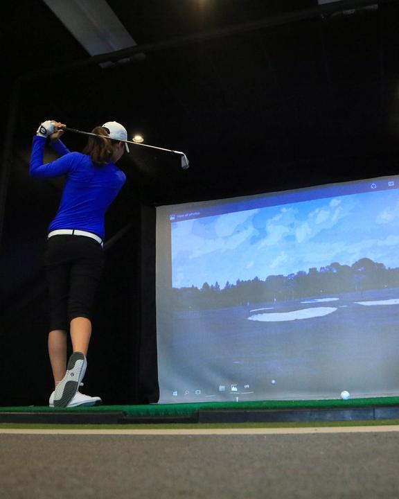 A golfer hitting into an indoor simulator