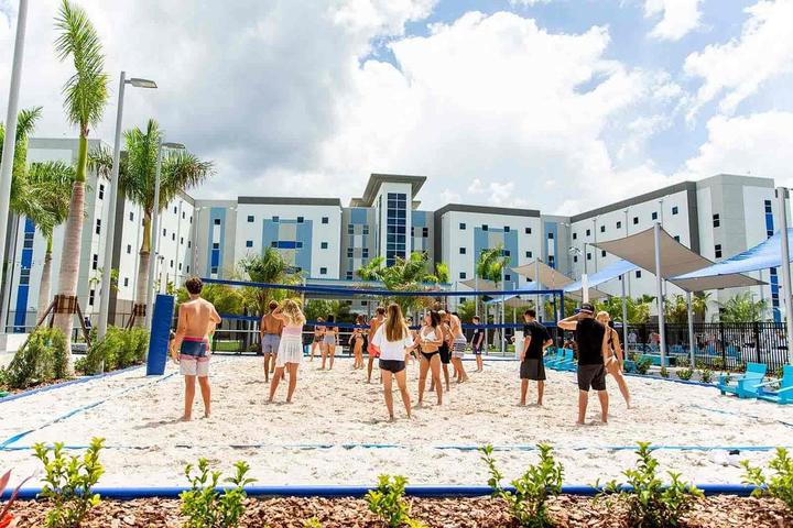 Campers playing beach volleyball on the sand courts in front of the residence halls