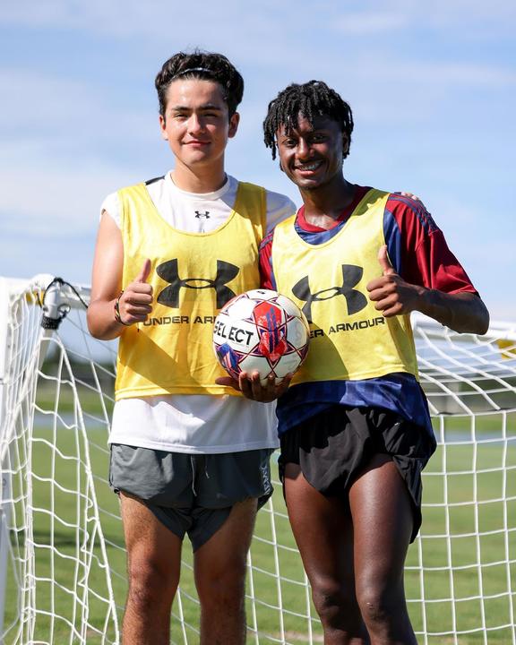 Two boys in training bibs giving a thumbs up in front of the goal