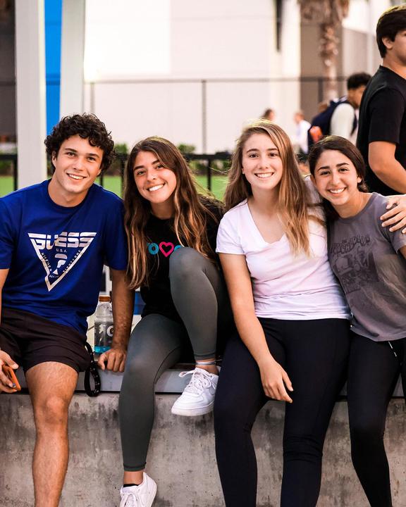 Four smiling teenagers sitting together on a wall
