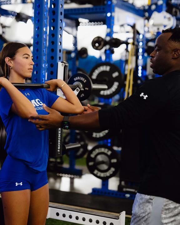 A coach checking a girl's form during a strength session