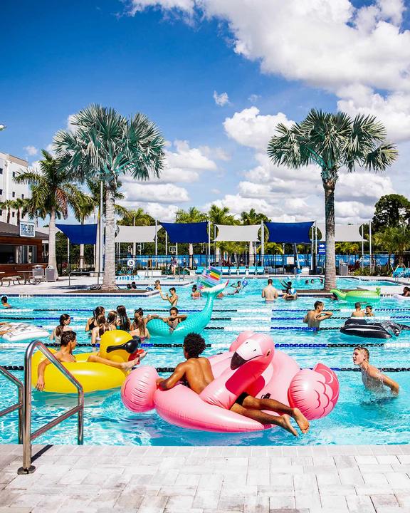 Campers on inflatable flamingos and ducks in the outdoor pool next to the residence halls