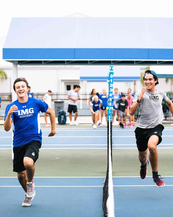 Two boys laughing as they sprint to the net in a footwork drill