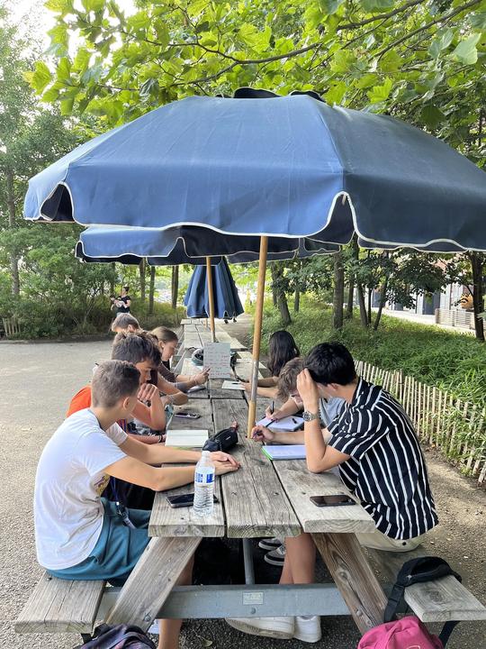 Small class at a picnic table under a parasol in a park